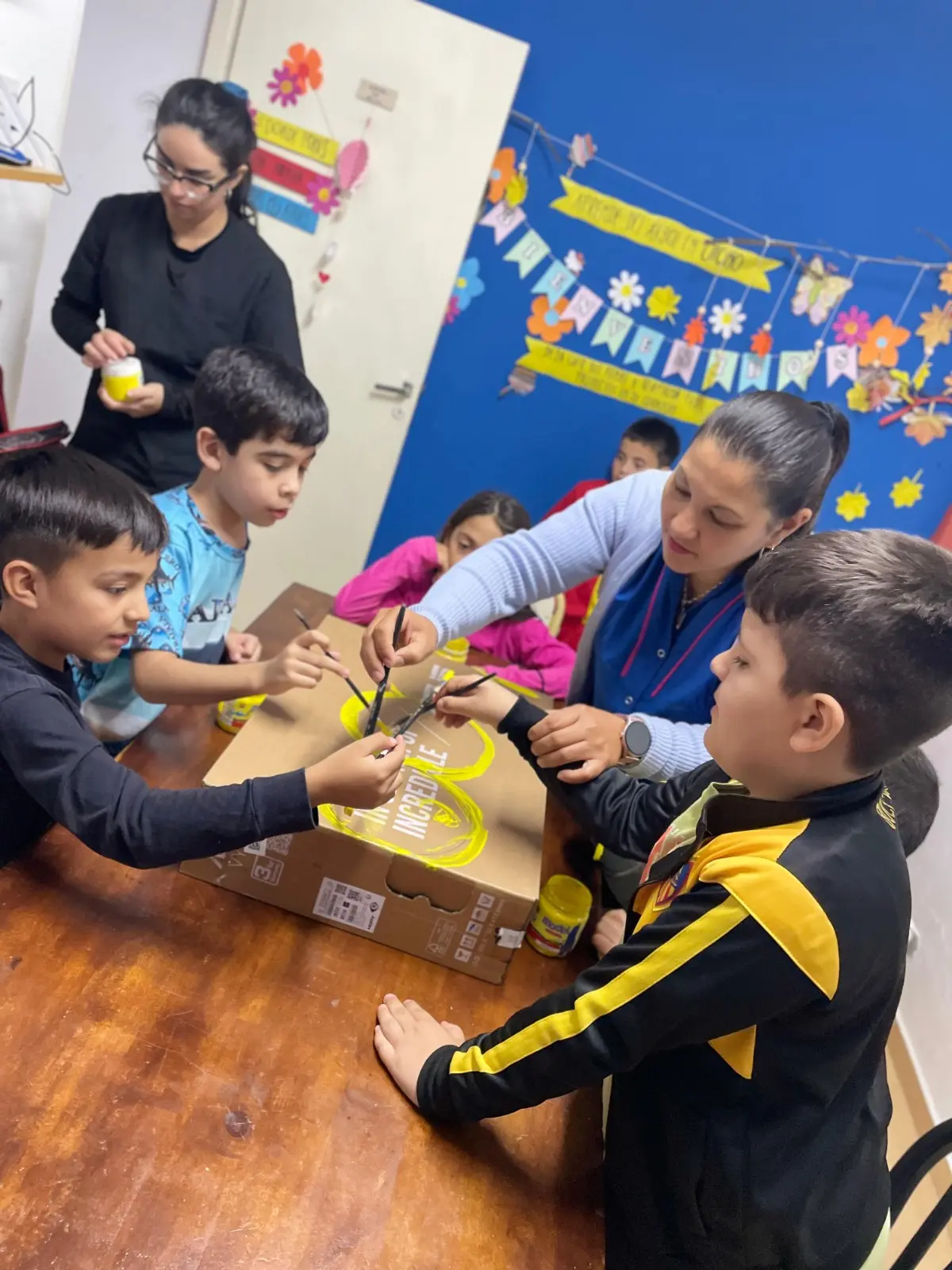 Niños pintando con témpera amarilla una caja de cartón