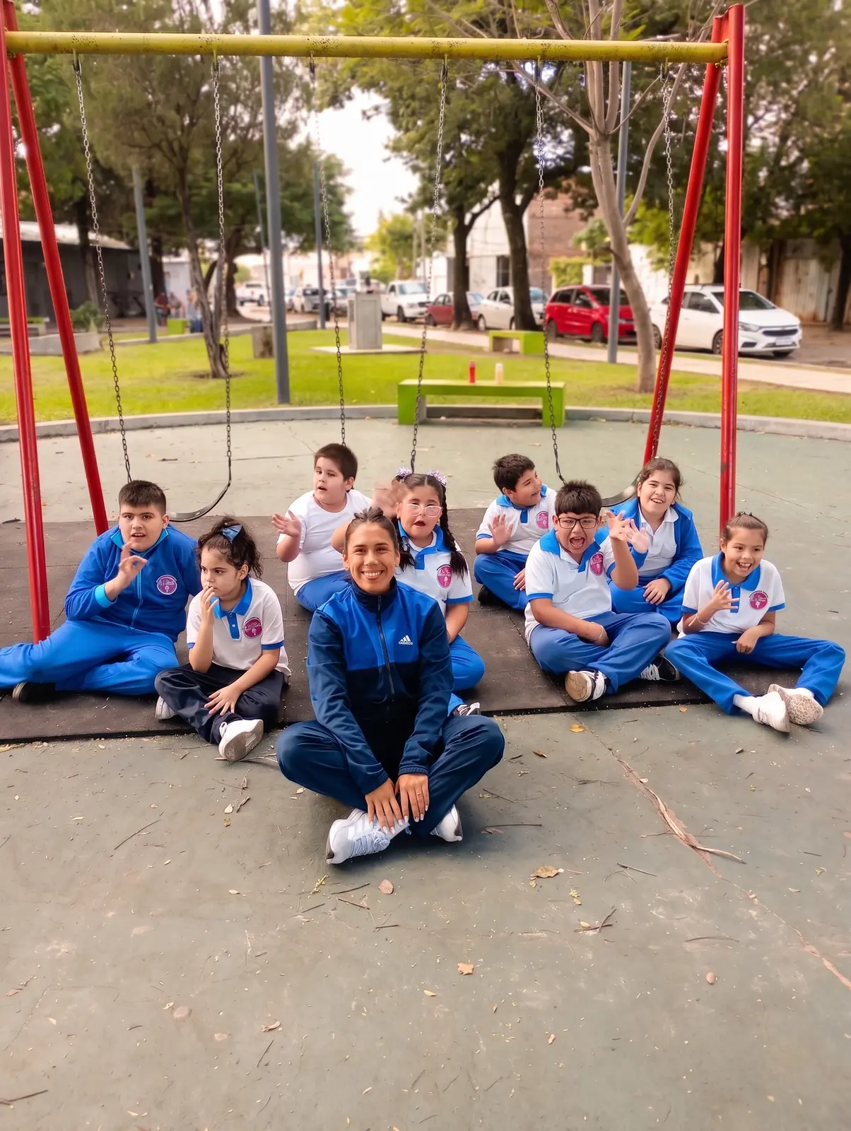 Niños sentados en la plaza junto a la profesora de educación física