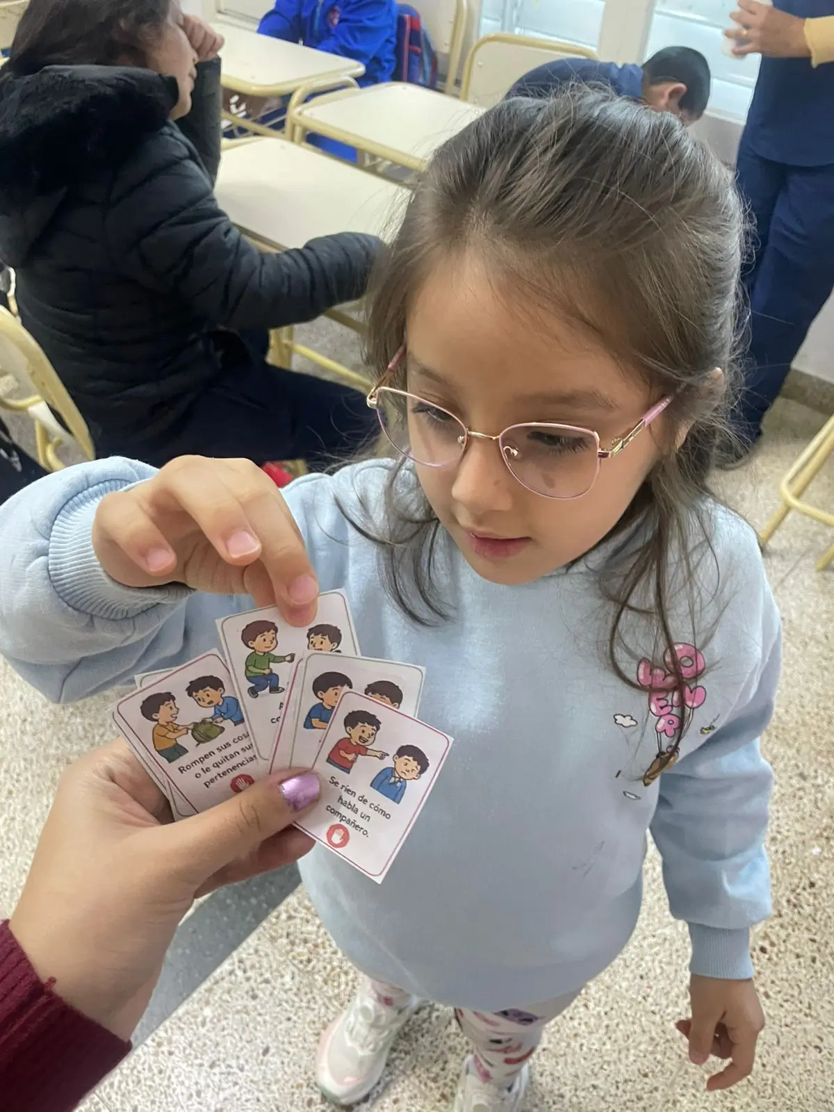 Niña con anteojos trabajando tarjetas de habilidades sociales